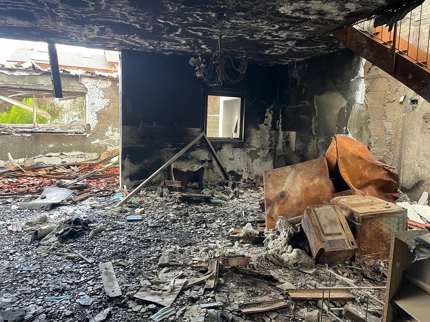 El interior incendiado de la casa de la familia Dvori en el kibutz Be’eri: techo y paredes negras, una lámpara colgando y escombros en el piso.