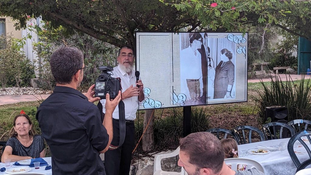 Roy Idan, de espaldas, filma con su cámara a un hombre que habla en el encuentro de la familia Mor, en un jardín de Kfar Aza.