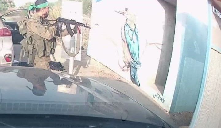 Un terrorista armado dispara hacia la entrada de un refugio junto a la ruta, visto desde el parabrisas de un auto.